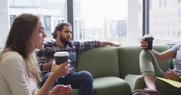 Diverse group of business colleagues sitting on sofa drinking coffee and talking