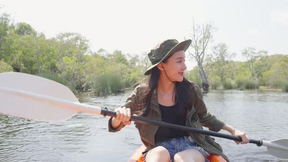 Asian young attractive tourist woman rowing kayak alone in forest lake.