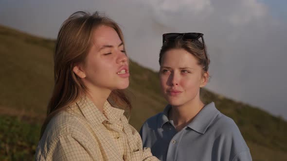 Two Young Female Friends are Chatting Standing on Slope of Mount at Summer