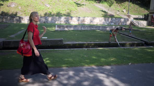 Beautiful mature woman in red ethnic, Thai dress walking in the dappled shade past a sign showing hi