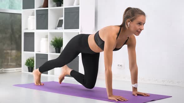 Barefoot Yoga Woman in Earphones Doing Exercise on Mat at White Home Interior