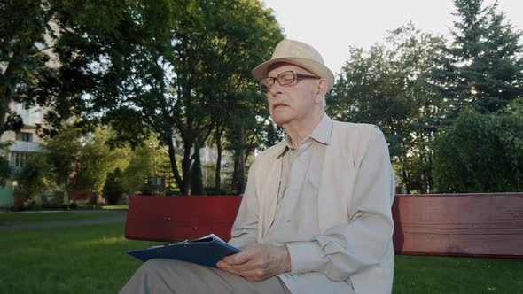 Elegant Mustachioed Senior Man Sitting on Park Bench Thinking and Noting