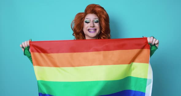 Happy drag queen holding rainbow flag while dancing inside the studio - Lgbtq concept