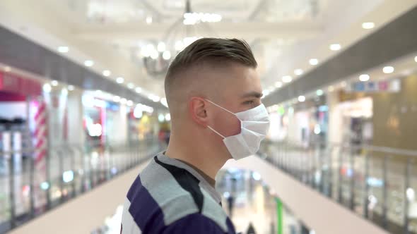 Young Man in a Medical Mask in a Shopping Center. A Man Stands with His Back, and Then Turns Around