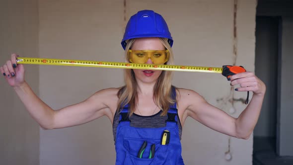 Young Beautiful Woman Builder or Worker Measures with a Construction Tape