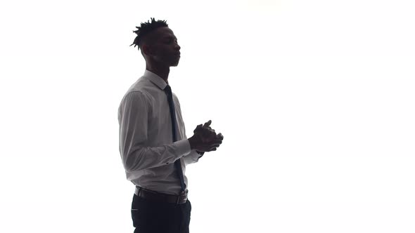 Black Man in Office Clothes Stands on White Background Rubs His Hands and Folds Them on His Chest