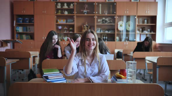 A Girl Student Sitting at a Desk Raises Her Hand in the Class