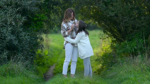 Loving tender mum hugging with a cute daughter on a field at sunset on a summer