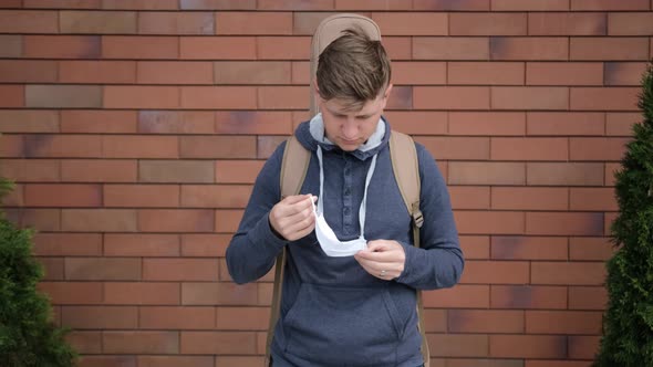 Caucasian Young Man with a Guitar on the Back Is Putting on a Medicinal Mask.