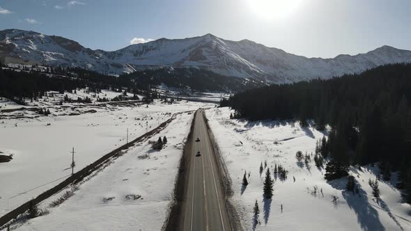 4k drone video of cars driving down road in winter in the Rocky Mountains in Colorado.