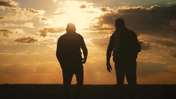 Silhouettes of Two Hikers with Backpacks Enjoying Sunset View From Top of a Mountain