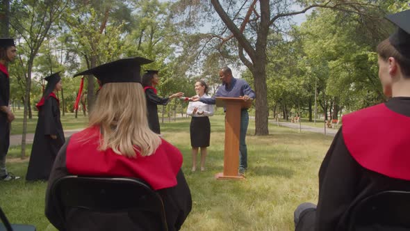 Happy Multiracial Graduates Receiving Diplomas From Dean at Graduation Day