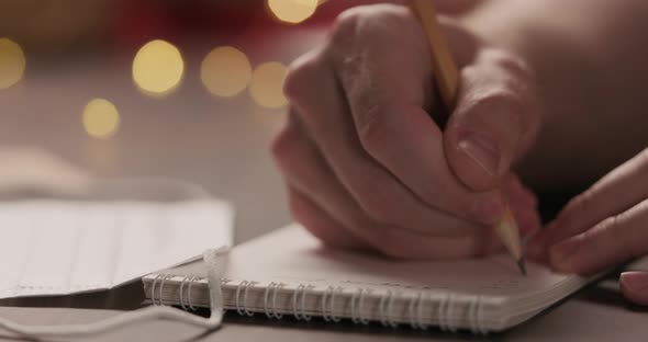 Slow Motion Closeup Man Writes Shopping List in Notepad with a Pencil Under Warm Light in the