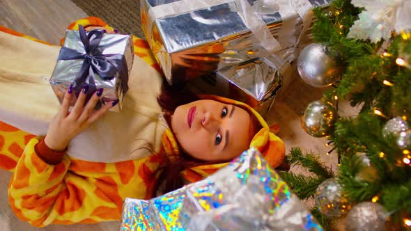 Woman in Pajamas Lying on Floor with Gift in Hands Near Christmas Tree