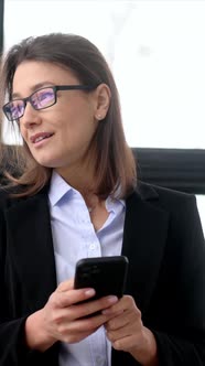 Vertical Video Intelligent Caucasian Business Lady in Suit and Glasses Uses Smartphone for Business