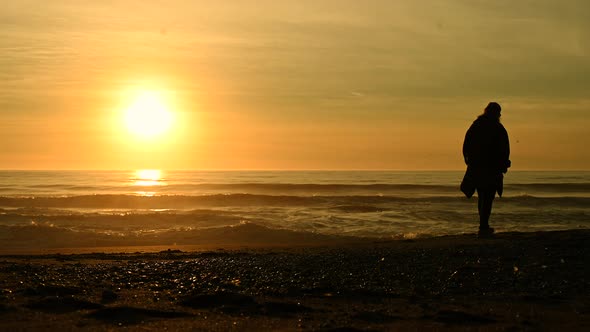 Woman Walking Alone Along the Beach During Scenic Sunset