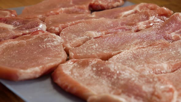 Pouring salt on fresh raw pork meat steaks in close up static view