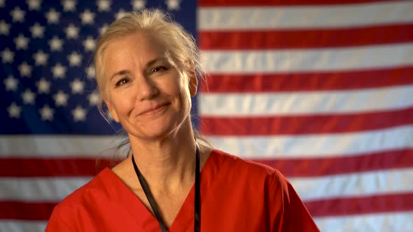 Female nurse walking from out of focus US flag to a medium tight portrait looking very relieved and