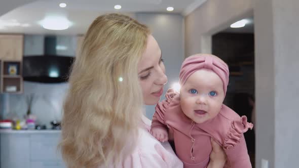 Mother Swings Baby in Her Arms on the Background of a Modern Kitchen Set