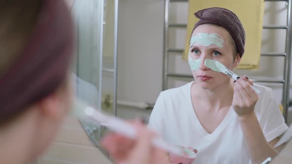 Young Mature Woman Applying Facial Clay Mask in Bathroom Spbas