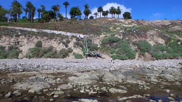 Aerial shot of a young man running stairs on the side of a cliff by the ocean.