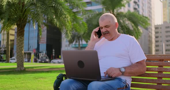 Senior Man Sitting in Park with Laptop in Summer and Chatting