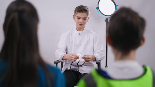 Smiling Teenage Caucasian Boy Sitting at White Background Explaining Medical Profession Choice