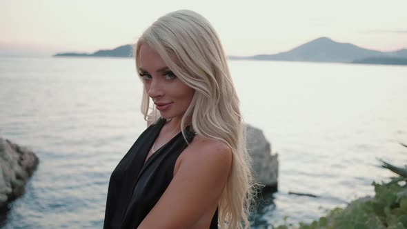 Beautiful  blonde woman  in black dress walking at sunset against the sea