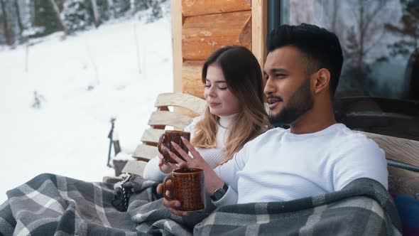 Happy Young Couple Hugging Covered with Blanket on the Outdoors Bench