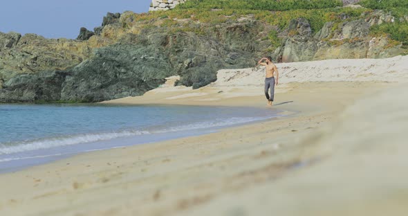 The Handsome Man with a Perfect Athletic Body in Gray Trousers Having Fun on a Deserted Beach in the