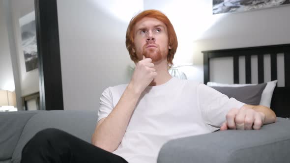 Pensive Redhead Man Thinking, Sitting on Couch in Bedroom