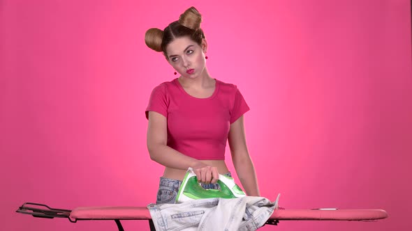 Teen Ironing Clothes with an Iron on a Pink Board. Pink Background. Slow Motion