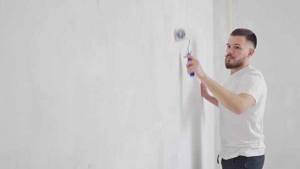 a Young Man with a Funny Mustache Paints the Wall with a Roller