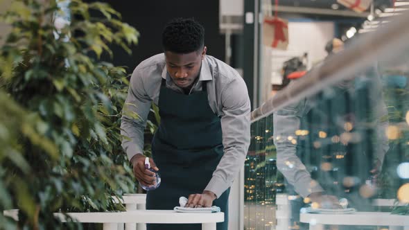 Young African American Student Waiter Catering Worker in Apron Wipes Table Splashing with