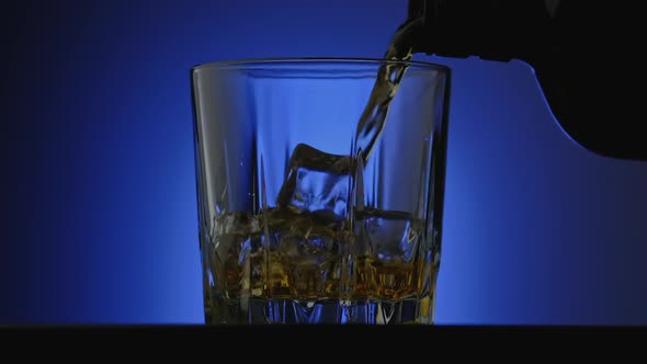 Close-up of Whiskey Pouring at Blue Background. Alcohol Pouring in Glass