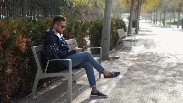 Casual Happy Man Using Smartphone Sitting on a Bench in Park Tourist Use Voice Recognition Ai Speech