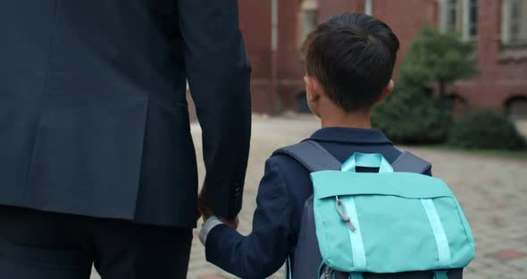 Close Up View of Kid Boy with Bag Taking His Father Hand and They Walking To School. Male Person in