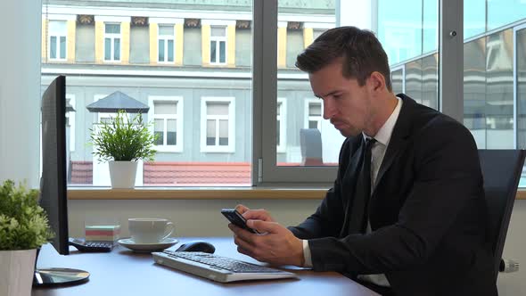 An office worker in a suit works on a computer and a smartphone