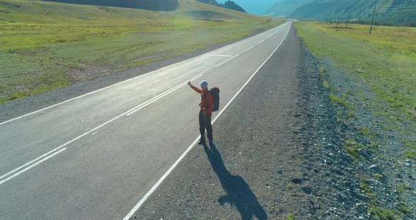 Flight Over Hitchhiker Tourist Walking on Asphalt Road. Huge Rural Valley at Summer Day. Backpack