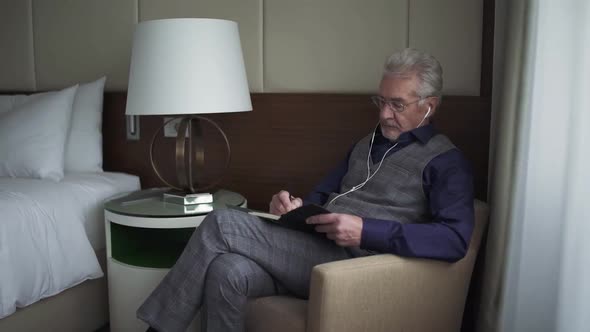Portrait of an Grayhaired Designer Sitting in a Hotel Room and Writing Down Thoughts in a Notebook