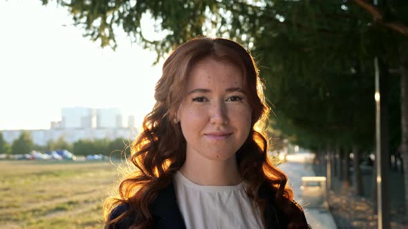 Portrait of Beautiful Young Woman with Red Hair Looking Up to the Camera and Smiling Charmingly