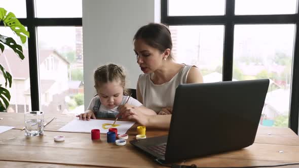 Young Woman Working with Laptop Remotely While Girl Drawing at Table in Home Interior Iroi