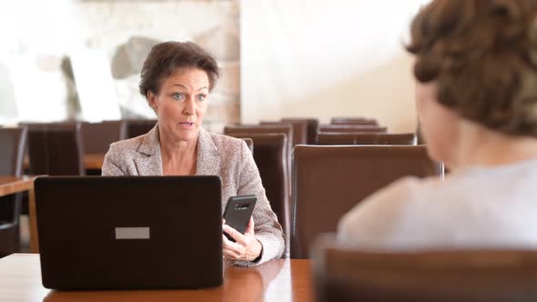 Happy Mature Businesswoman Using Technology While Talking With Senior Woman