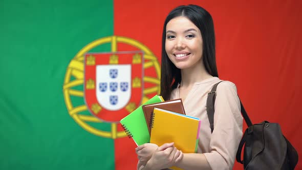 Asian Female Student Holding Copybooks Against Portuguese Flag Background