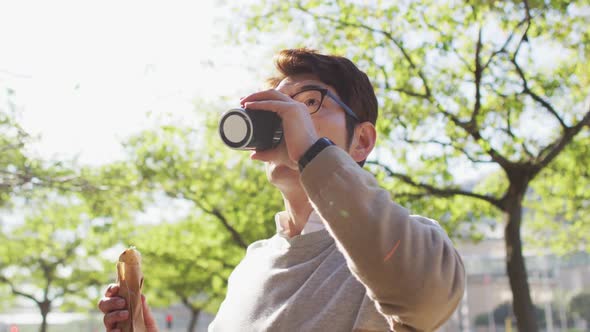 Asian man drinking coffee and having a snack while walking outdoors