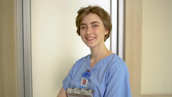 Cheerful young female professional medical nurse standing in modern hospital and smiling to camera