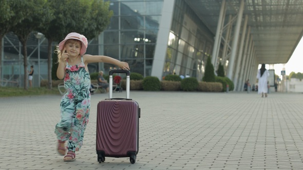 Child Girl Tourist with Suitcase Bag Near Airport. Kid Dances, Rejoices, Celebrates with Luggage