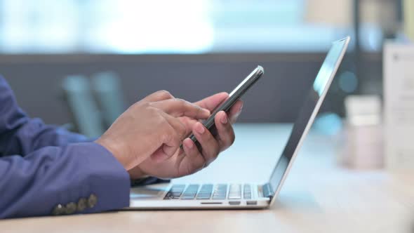 Close Up of Hands of African Businessman with Laptop Using Smartphone