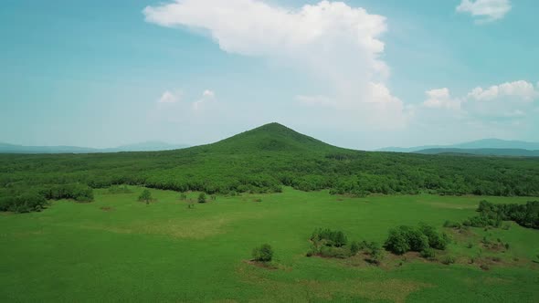 Aerial View of an Endless Geen Meadow and a Hill Against the Blue Sky with Clouds