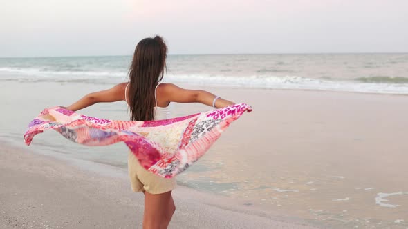 A Girl in a Summer Tshirt and Shorts is Walking Along the Beach Looking at the Horizon and Holding a